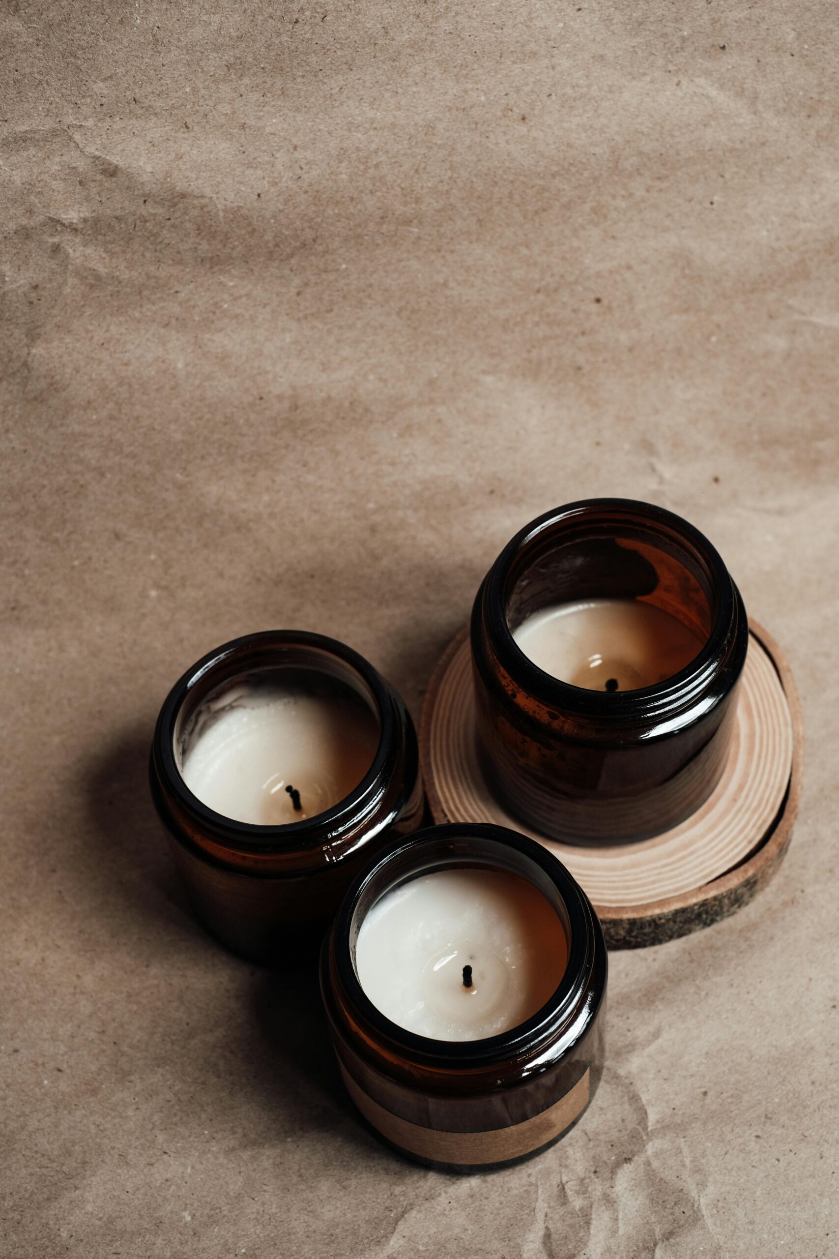 Three scented candles in amber glass jars arranged on a wooden slice, creating a cozy atmosphere.